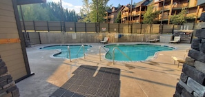 A pool area with two pools, lounge chairs, and a stone wall.