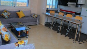 Een woonkamer met een bank, een glazen salontafel en een eethoek met een tafel en stoelen.