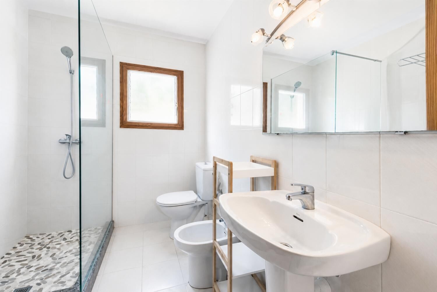 Een moderne badkamer met een douchecabine van glas, een wit toilet, een wastafel op voetstuk en een grote spiegel.