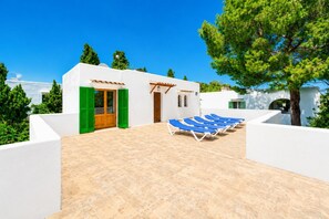 Un bâtiment moderne à l’extérieur blanc, doté d’une porte en bois et d’un patio carrelé agrémenté de chaises longues bleues.
