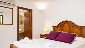 A hotel room with a wooden bed, a nightstand with a lamp, a bathroom visible through an open door, and a mirror on the wall. - Villa Binimelis - Five Bedroom Villa, Sleeps 10 (Cala d'Or)