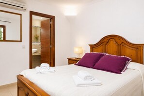Ein Hotelzimmer mit einem hölzernen Bett, einem Nachttisch mit Lampe, einem durchgegangenen Badezimmer und einem Spiegel an der Wand.