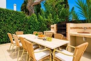 Ein Essbereich im Freien mit Tisch und Stühlen, einem Grill und einem Spülbecken.