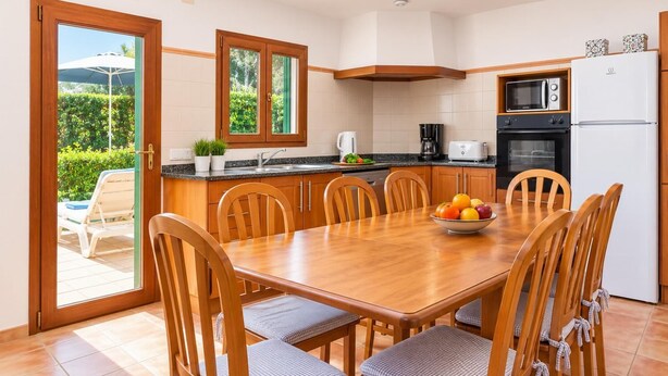 A modern kitchen with a dining table, chairs, and a fruit bowl. - Villa Binimelis - Five Bedroom Villa, Sleeps 10 (Cala d'Or)