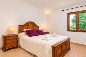 Une chambre d’hôtel avec un lit en bois, deux tables de chevet, une fenêtre donnant sur un paysage verdoyant et un sol carrelé.