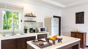 A modern kitchen with a large island, dark wood cabinets, a white countertop, a refrigerator, a microwave, and a window with a view of greenery. - Beautiful villa with swimming pool (Tambon Rawai)