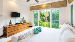 A bedroom with a bed, a wooden dresser, a television, and a view of greenery through the window. - Beautiful villa with swimming pool (Tambon Rawai)