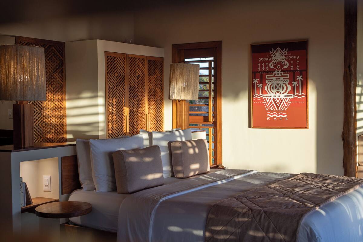 A bed with a patterned bedspread, a nightstand, a lamp, and a wall with a geometric design.