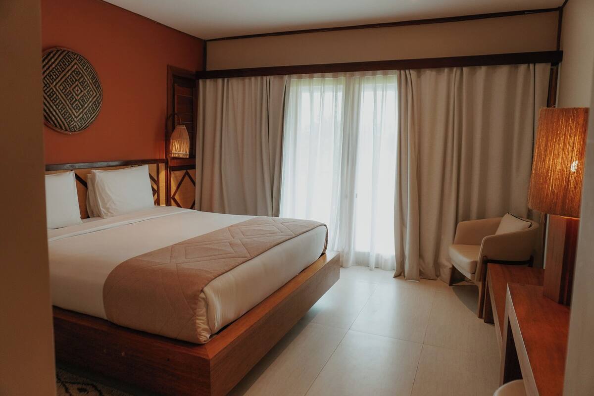 A hotel room with a large bed, a chair, a desk, and a lamp.