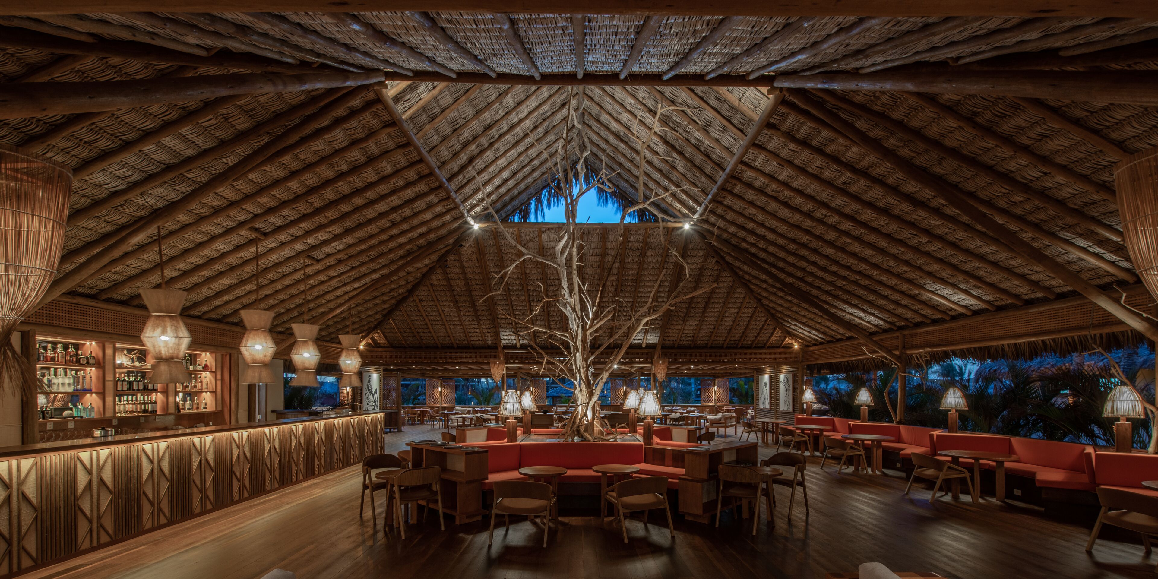 An indoor space with a high thatched roof, wooden furniture, and a bar area with shelves of bottles.