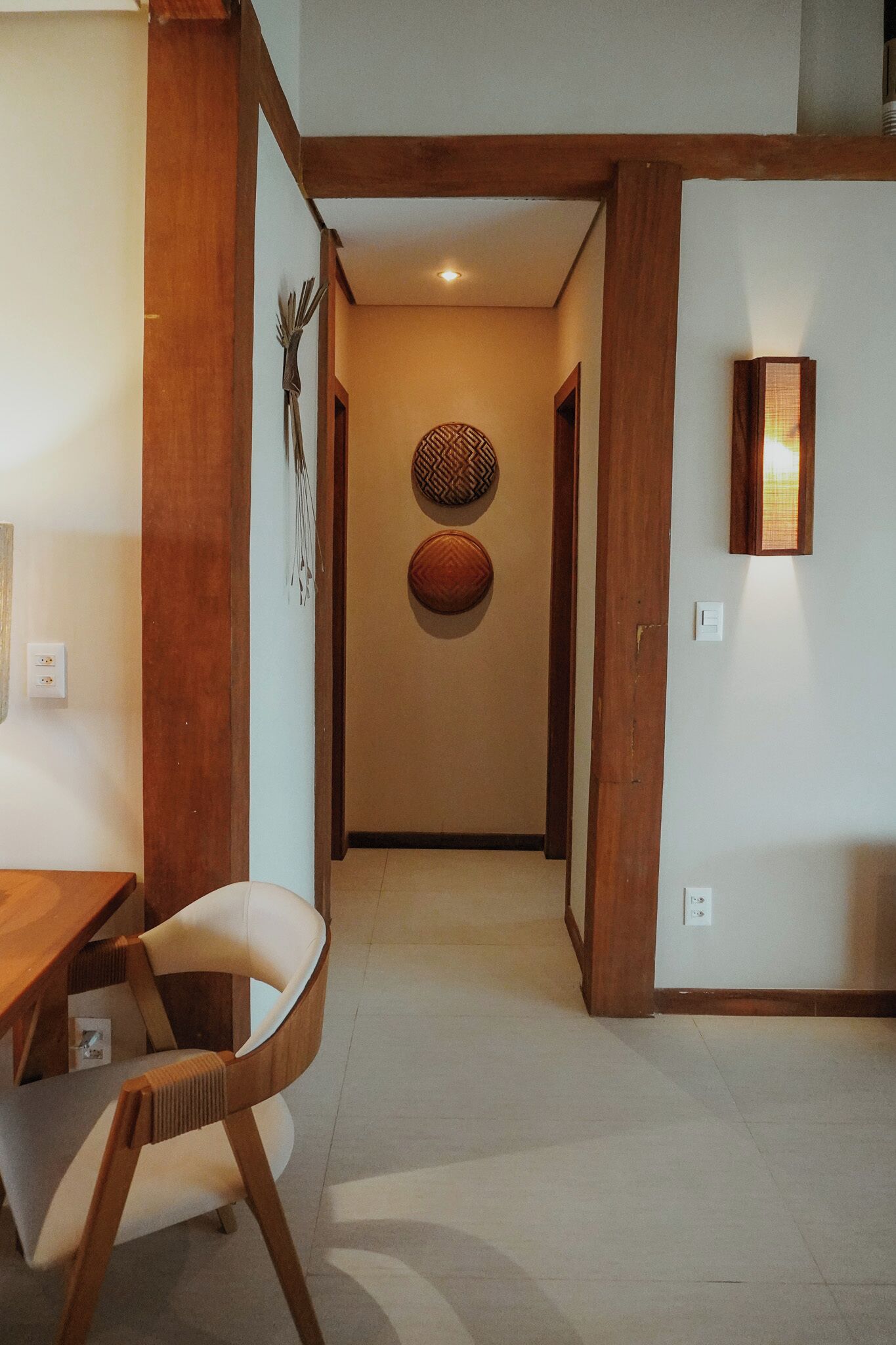 A hallway with a wooden door, a dining area with a table and chairs, and a wall-mounted light fixture.