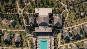 Vista aérea de un resort con una piscina central, varias cabañas y acceso a la playa.