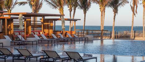 A poolside area with lounge chairs and a wooden pergola overlooking the ocean.