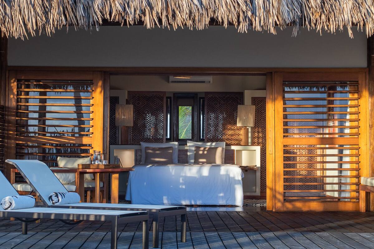 A thatched-roof bungalow with a wooden deck, a sofa, and a table.