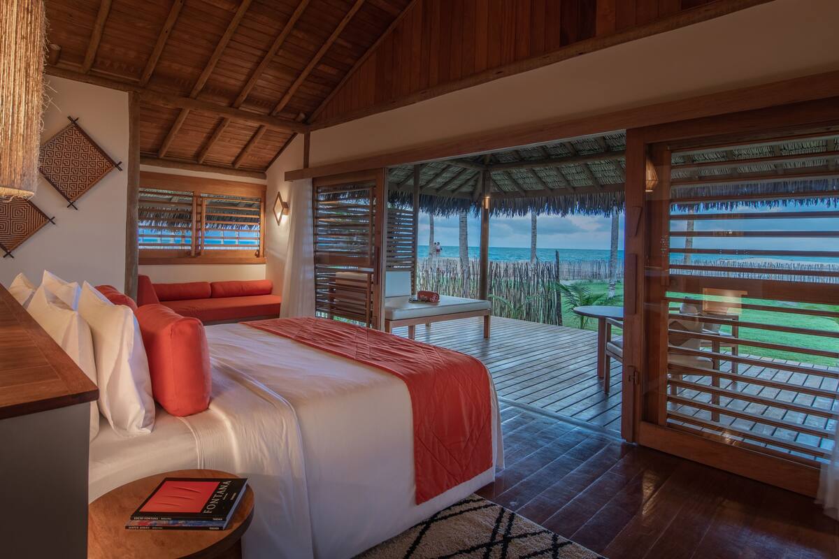 A bedroom with a large bed, a wooden desk, and a view of the beach through a sliding door.