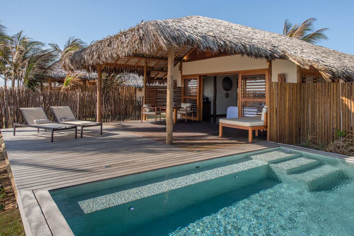 A poolside area with a thatched-roof structure, lounge chairs, and a wooden deck.