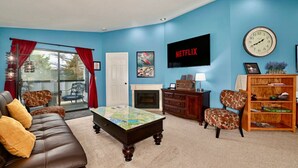 A living room with a brown leather sofa, a coffee table, a fireplace, a bookshelf, and a TV mounted on the wall. - Fishy-Fishy Townhome, 2BR/2BA (Kenai)