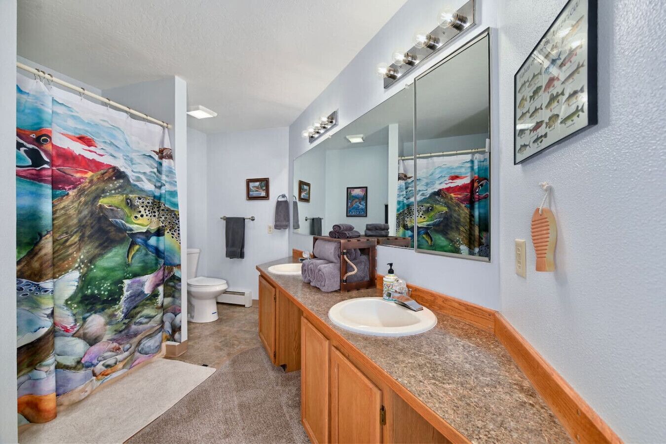 Un baño con un espejo grande, dos lavamanos, una cortina de ducha con diseño de peces y un cuadro de peces enmarcado en la pared.