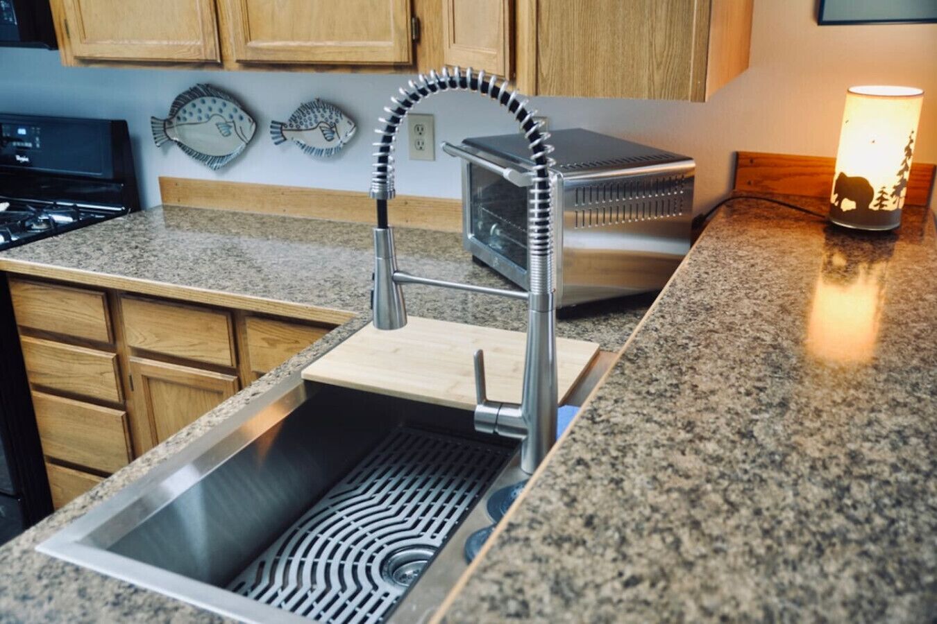 Una cocina con pileta de acero inoxidable, grifo moderno, alacenas de madera y encimera de granito.