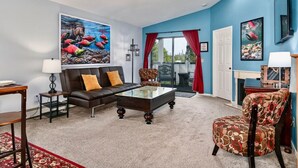 A living room with a sofa, coffee table, patterned armchair, and a painting of fish on the wall. - Fishy-Fishy Townhome, 2BR/2BA (Kenai)