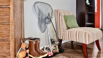 A room with a striped armchair, a green pillow, a fishing net, fishing rods, and a pair of brown boots.