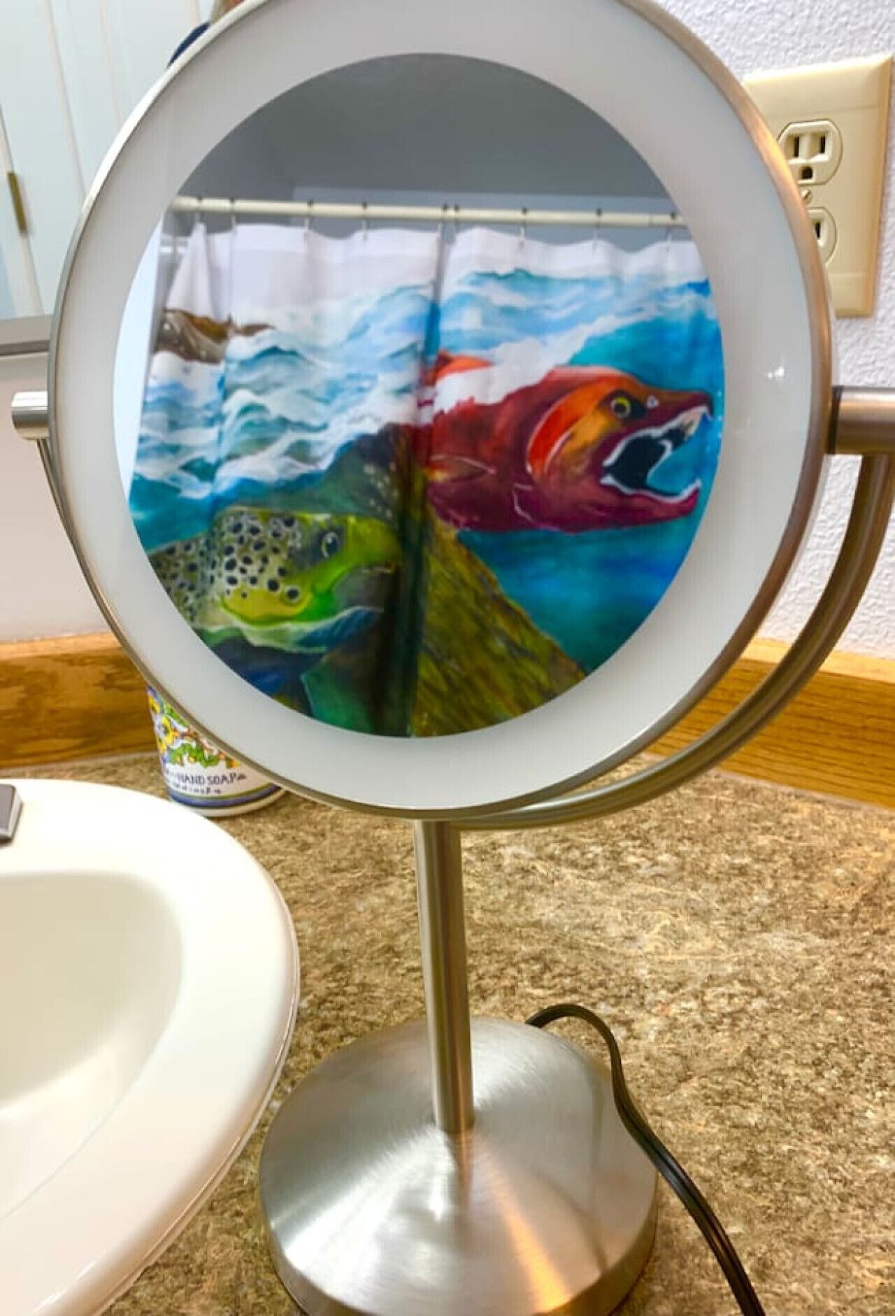 Un bagno con uno specchio tondo, un lavandino bianco e una bottiglia di sapone per le mani.