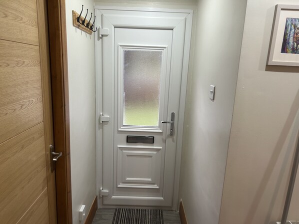 A narrow hallway with a wooden door on the left, a white door with a frosted glass window in the center, and a framed picture on the right wall. - Bright Star Lodge (Invergarry)