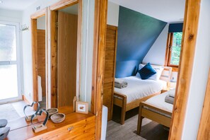 Une chambre à coucher avec un lit, une table de chevet et une fenêtre. On y trouve une porte en bois et un petit cadre photo posé sur le sol.