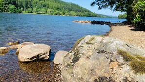 A clear lake with rocky shores and a forested hillside in the background. - Bright Star Lodge (Invergarry)
