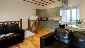 A modern kitchen with wooden beams, a dining area with a white table, and a leather sofa. - Stable Cottage (Port Isaac)