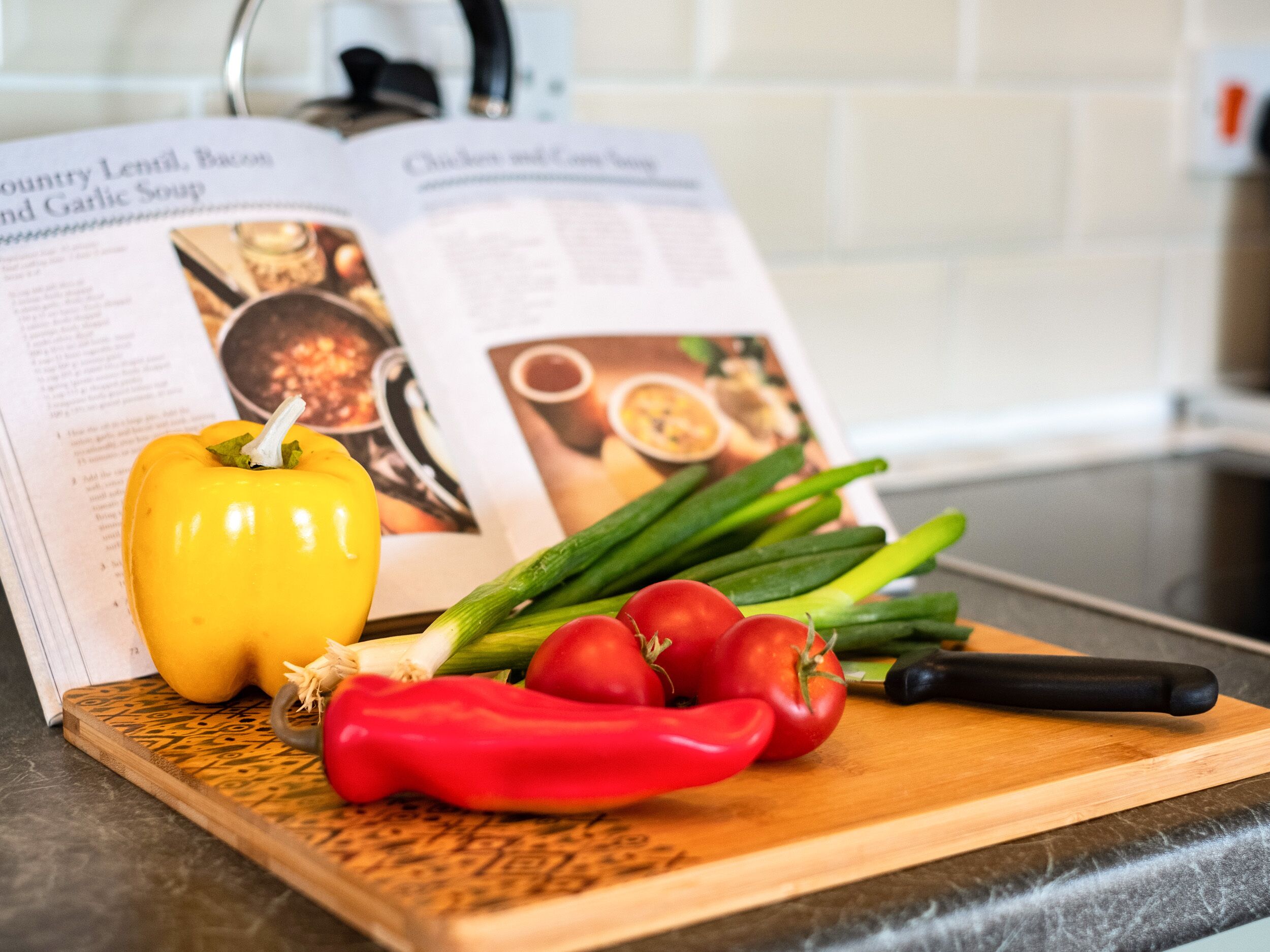 A kitchen counter with a cutting board holding vegetables and a cookbook.