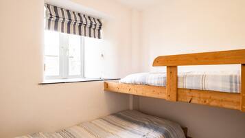 A small, single-room with a bunk bed and a single bed. There is a window with a striped valance and a view of the outside.
