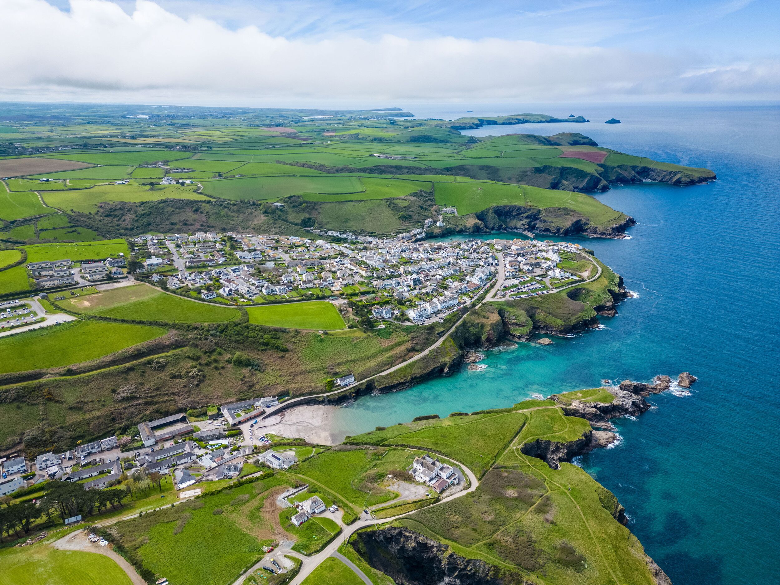 An aerial view of a coastal town with residential areas, green fields, and a coastline.