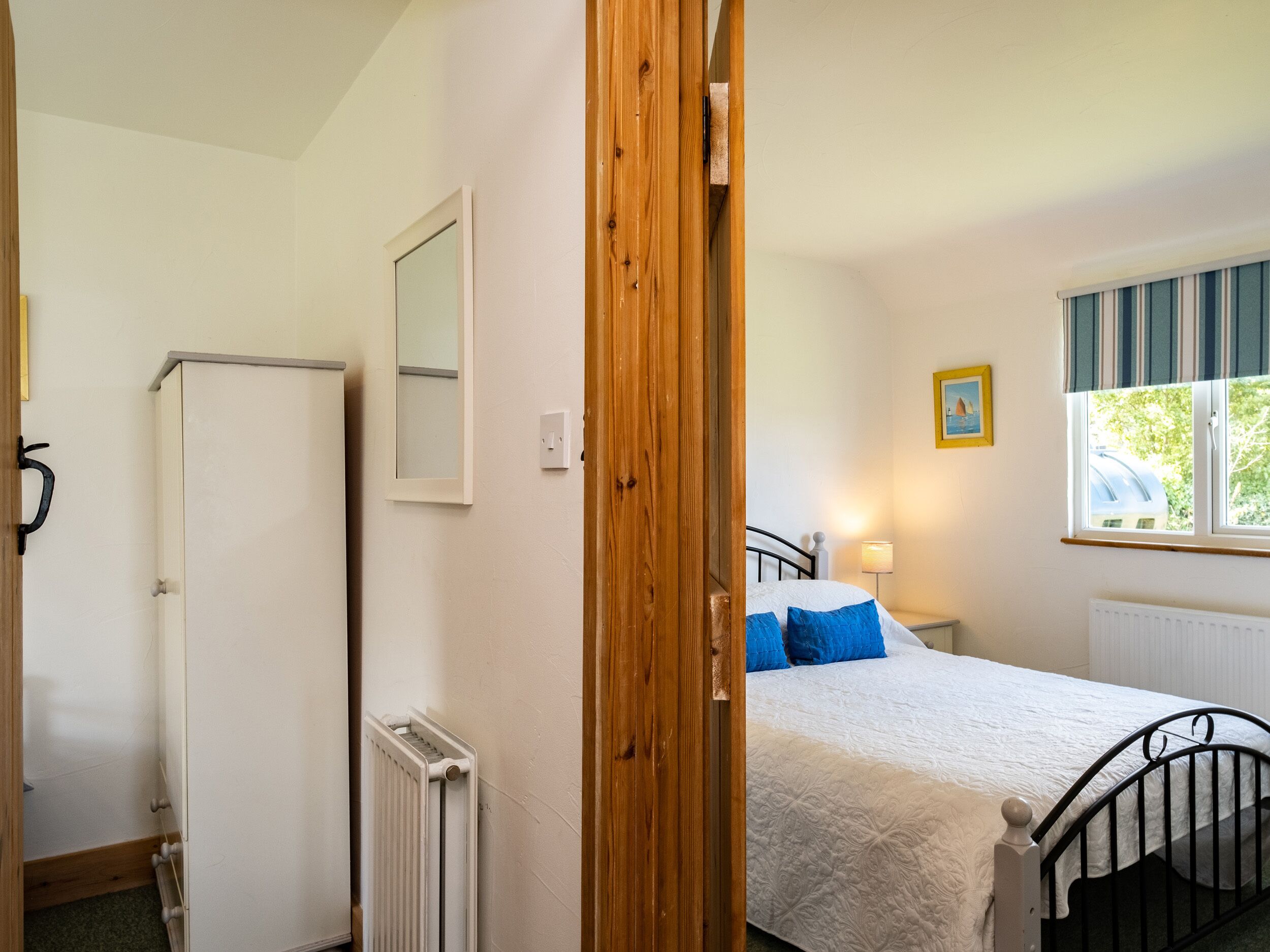 A bedroom with a bed, a radiator, a wooden door, a window, and a picture on the wall.