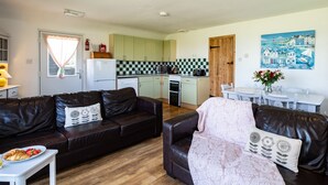 A compact living space with a kitchenette, a dining area, and a living room furnished with leather sofas and a coffee table. - Atlantic Lodge (Port Isaac)