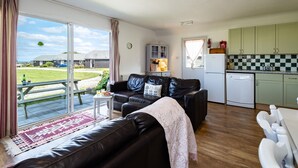 A cozy living room with a leather sofa, a dining table, and a kitchen area with green cabinets and a white refrigerator. - Atlantic Lodge (Port Isaac)