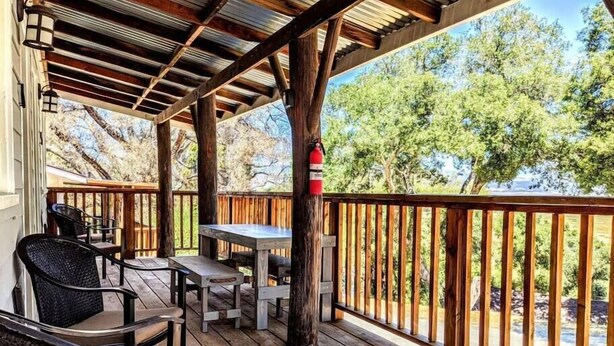 A covered outdoor area with wooden furniture, a fire extinguisher, and a view of trees and a body of water. - # 5. The Tipsy Turkey's Den - 1 Bedroom with Amazing Views (San Diego County)
