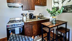 A compact kitchen with wooden cabinets, a gas stove, a sink, and a small table with stools. - # 5. The Tipsy Turkey's Den - 1 Bedroom with Amazing Views (San Diego County)
