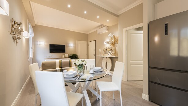A modern kitchen with a stainless steel refrigerator, a dining area with a glass table and white chairs, and a flat-screen TV mounted on the wall. - Michelangelo Hideaway by Mmega (Florence)