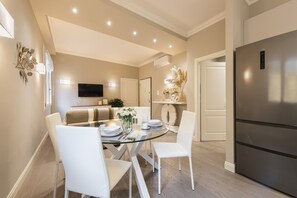 A modern kitchen with a stainless steel refrigerator, a dining area with a glass table and white chairs, and a flat-screen TV mounted on the wall. - Michelangelo Hideaway by Mmega (Florence)