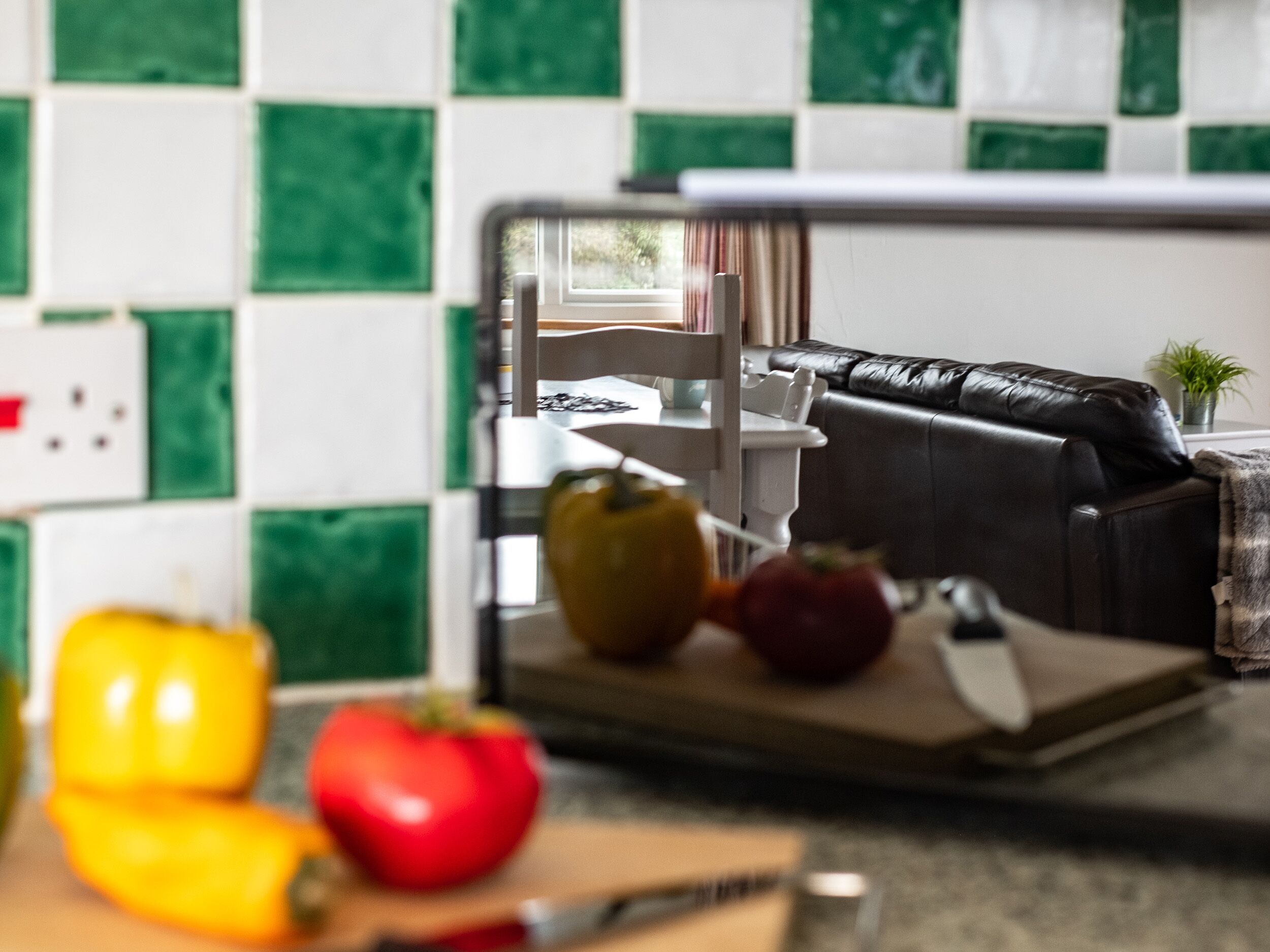 A kitchen with a cutting board, vegetables, and a black leather sofa in the background.
