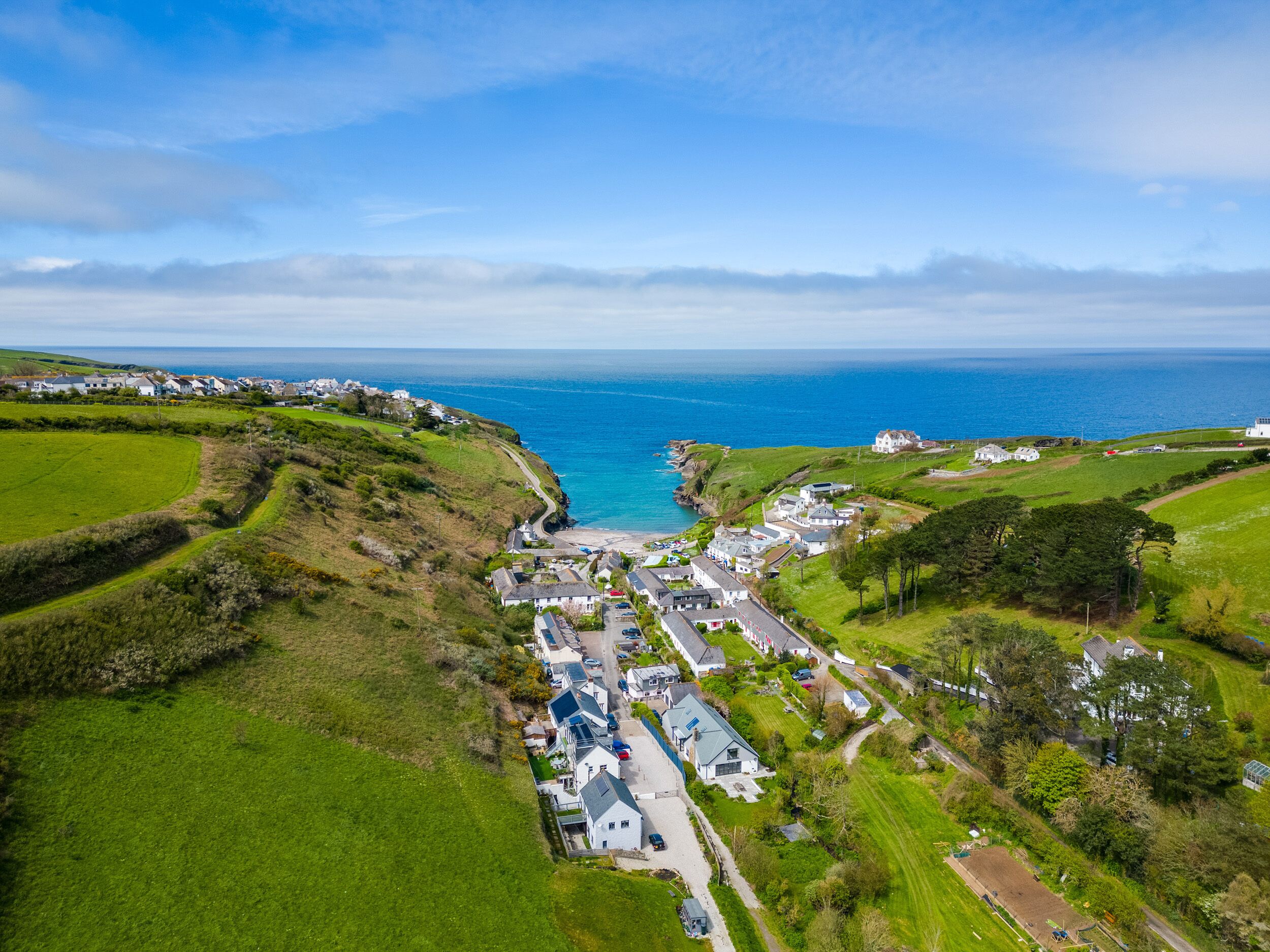 A coastal village with houses along the sea, a main road, and green fields.