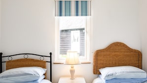 A bedroom with two single beds, a nightstand with a lamp, a window with striped curtains, and a view of the outside.