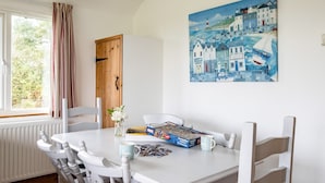 A dining area with a white table, chairs, a jigsaw puzzle, and a painting of a coastal scene.
