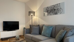 Een moderne woonkamer met een flatscreen televisie, een grijze bank, een salontafel en een vloerlamp.