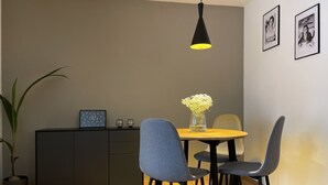 Een moderne eetruimte met een houten tafel, grijze stoelen, een zwart hanglamp en een kast met een fotolijst.