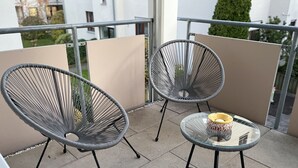 Een balkon met twee metalen stoelen en een glazen tafel, met een schaal en een kop.