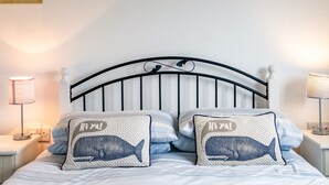 A bed with two whale-themed pillows, a white headboard, and bedside lamps. - Puffin Lodge (Port Isaac)