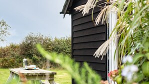 A wooden picnic table with a kettle and a cup, set on a grassy lawn in front of a black wooden building. - Puffin Lodge (Port Isaac)
