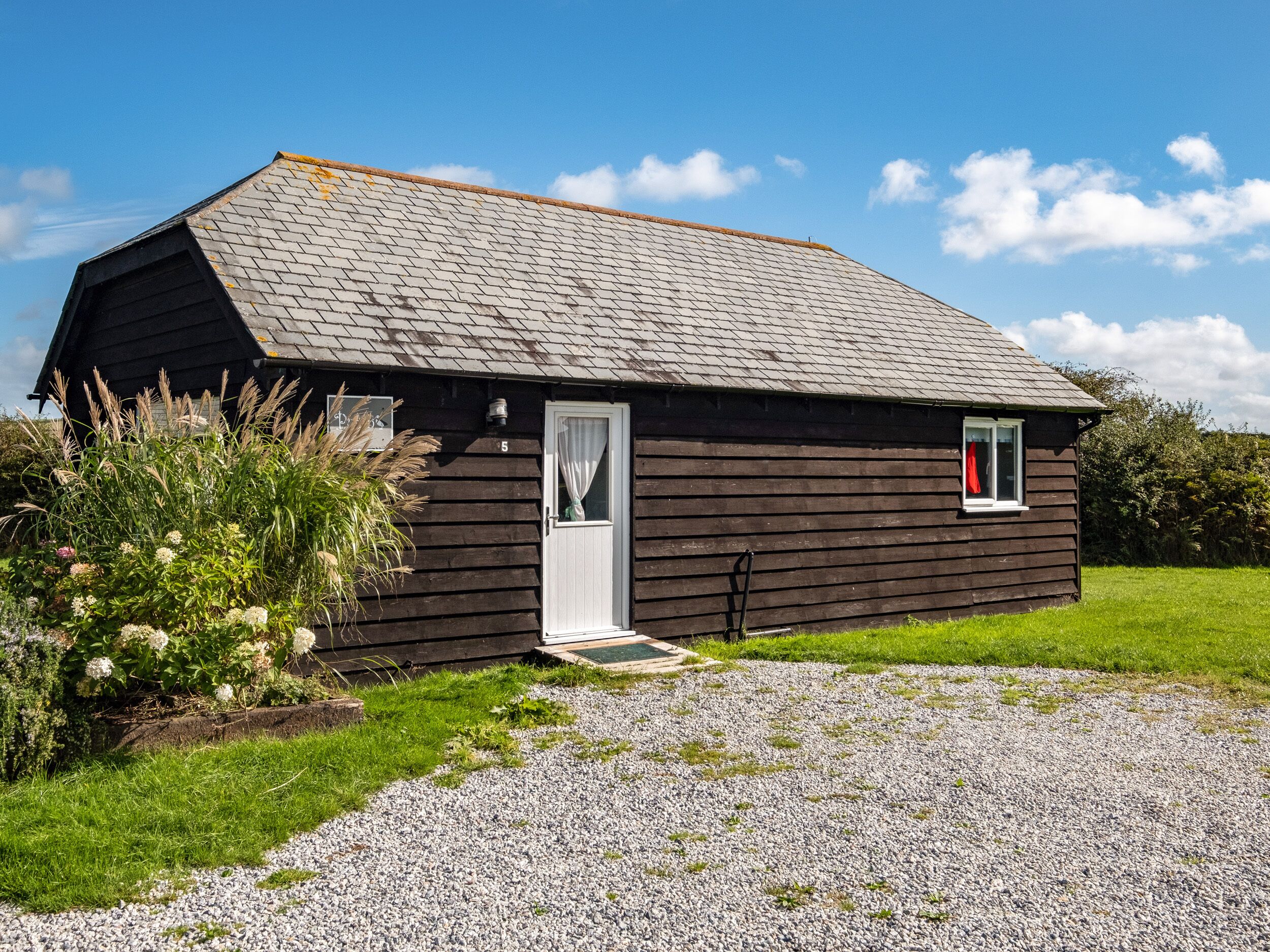A small, dark wooden house with a sloped roof, a white door, and a small window with a red curtain.